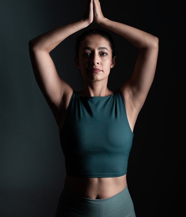 Woman in a calm yoga pose against a dark background with cyan light.